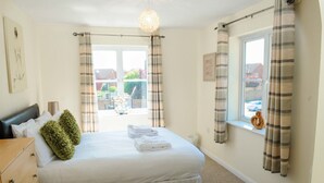 A neatly made bed with pillows and folded towels, a wooden dresser, a window with curtains, and a view of the outside. - Your Stay Bristol Orchard Gate (Bristol)