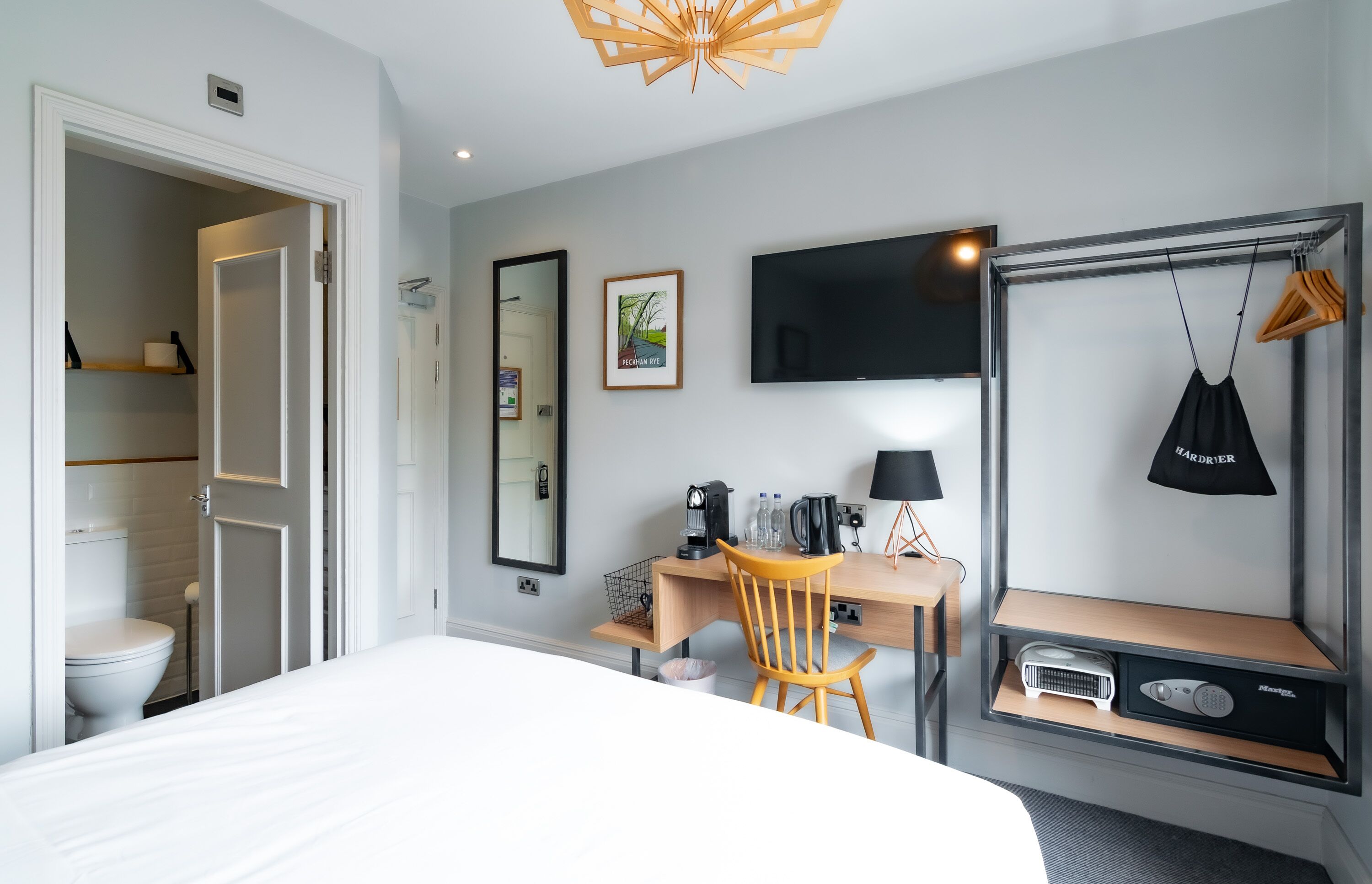 Une chambre d’hôtel comprenant un lit, un bureau avec une chaise, une télévision, un miroir et une armoire.