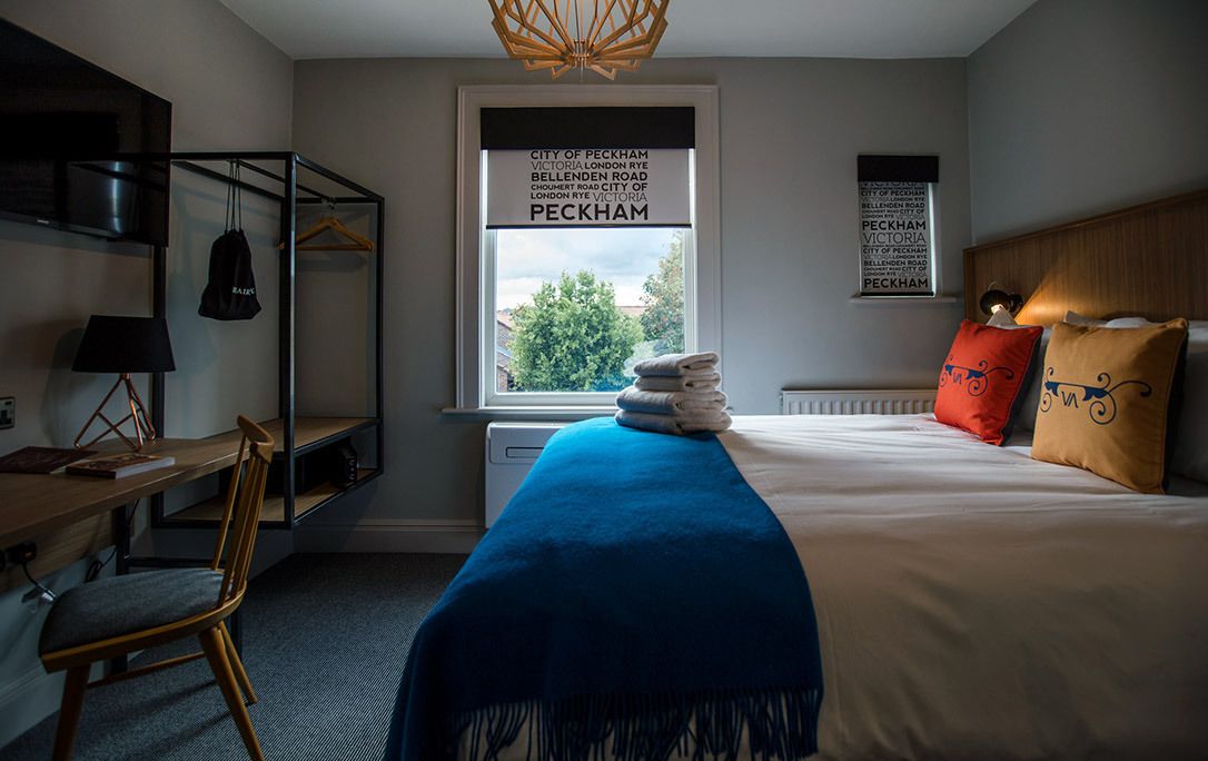 A bedroom with a bed, a desk, a chair, a radiator, and a window with a view of trees.