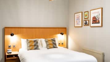 Una habitación de hotel moderna con una cama grande, cabecera de madera, una lámpara colgante geométrica singular y cuadros en la pared.