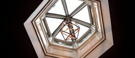 Une lucarne dotée d’un cadre métallique aux motifs géométriques et d’un luminaire central.