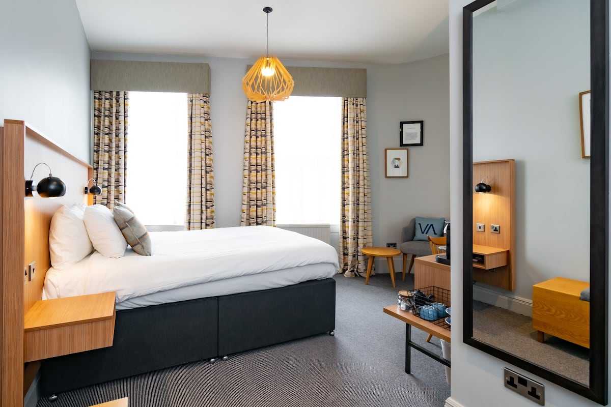 A modern bedroom with a bed, bedside tables, a desk, and a mirror.