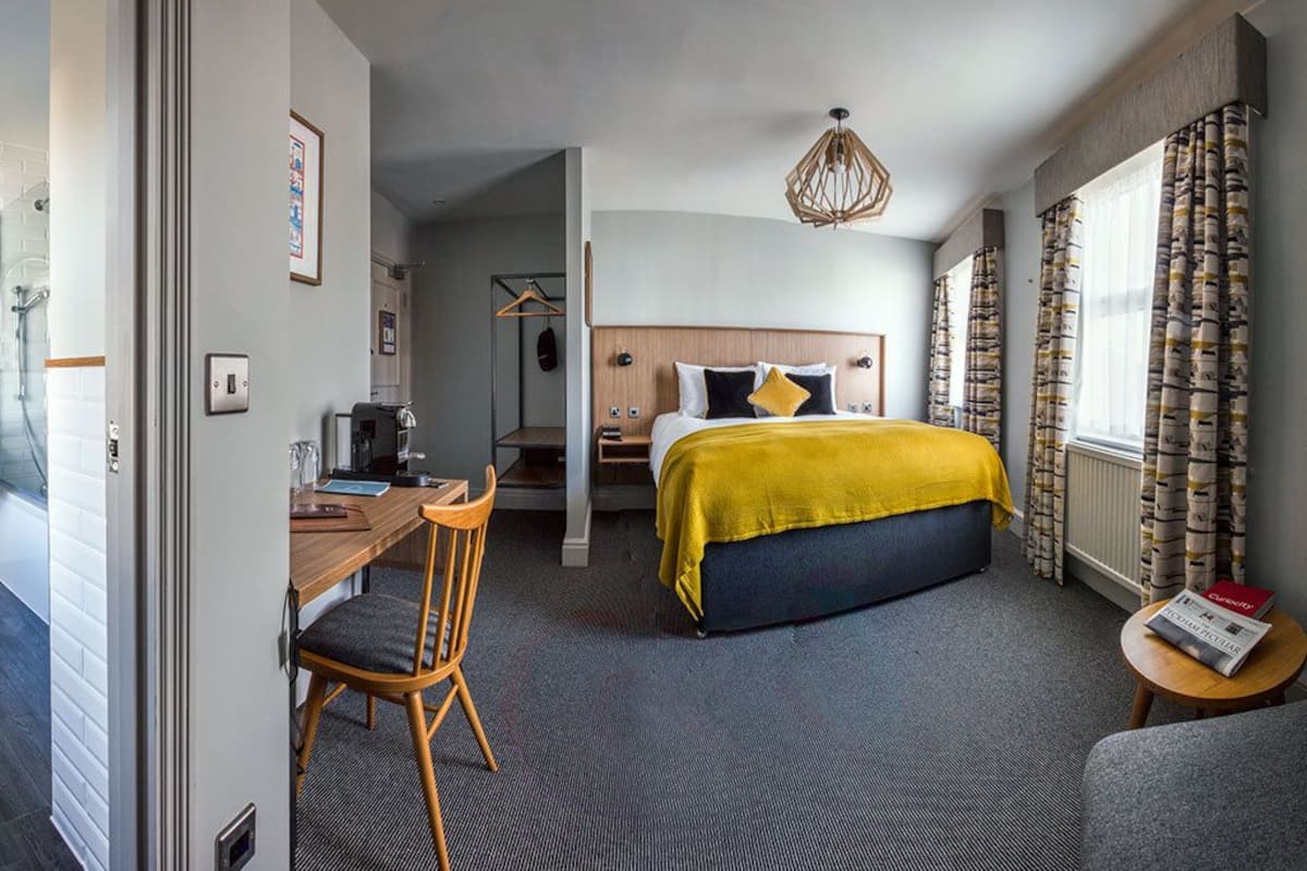 A hotel room with a bed, a desk, a chair, a small table, and a window with curtains.