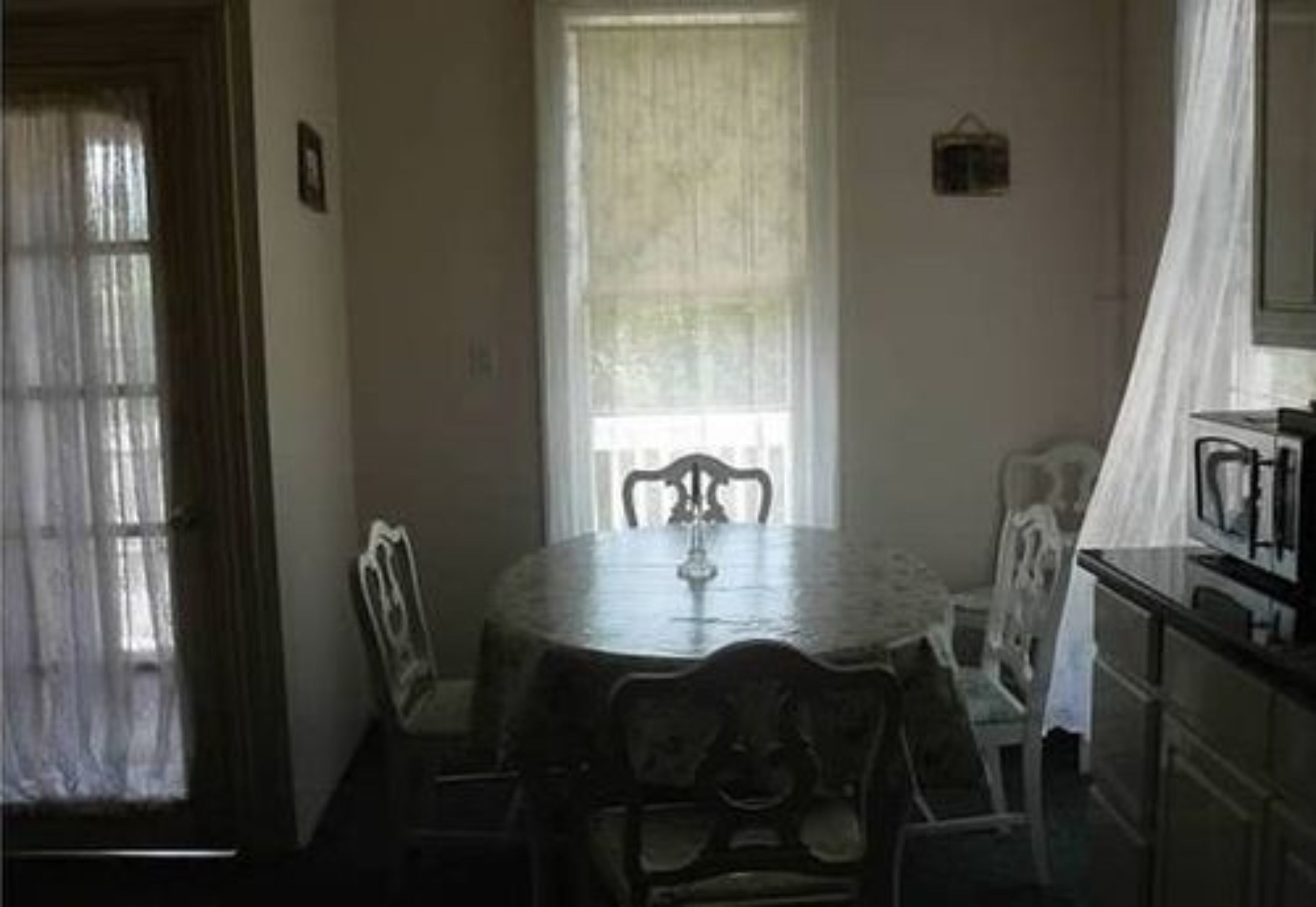 A dining area with a round table and chairs, a window with curtains, and a kitchen area with cabinets.