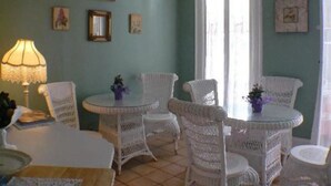 Une pièce avec une table ronde et des chaises en osier blanc, une lampe et des tableaux encadrés accrochés au mur.