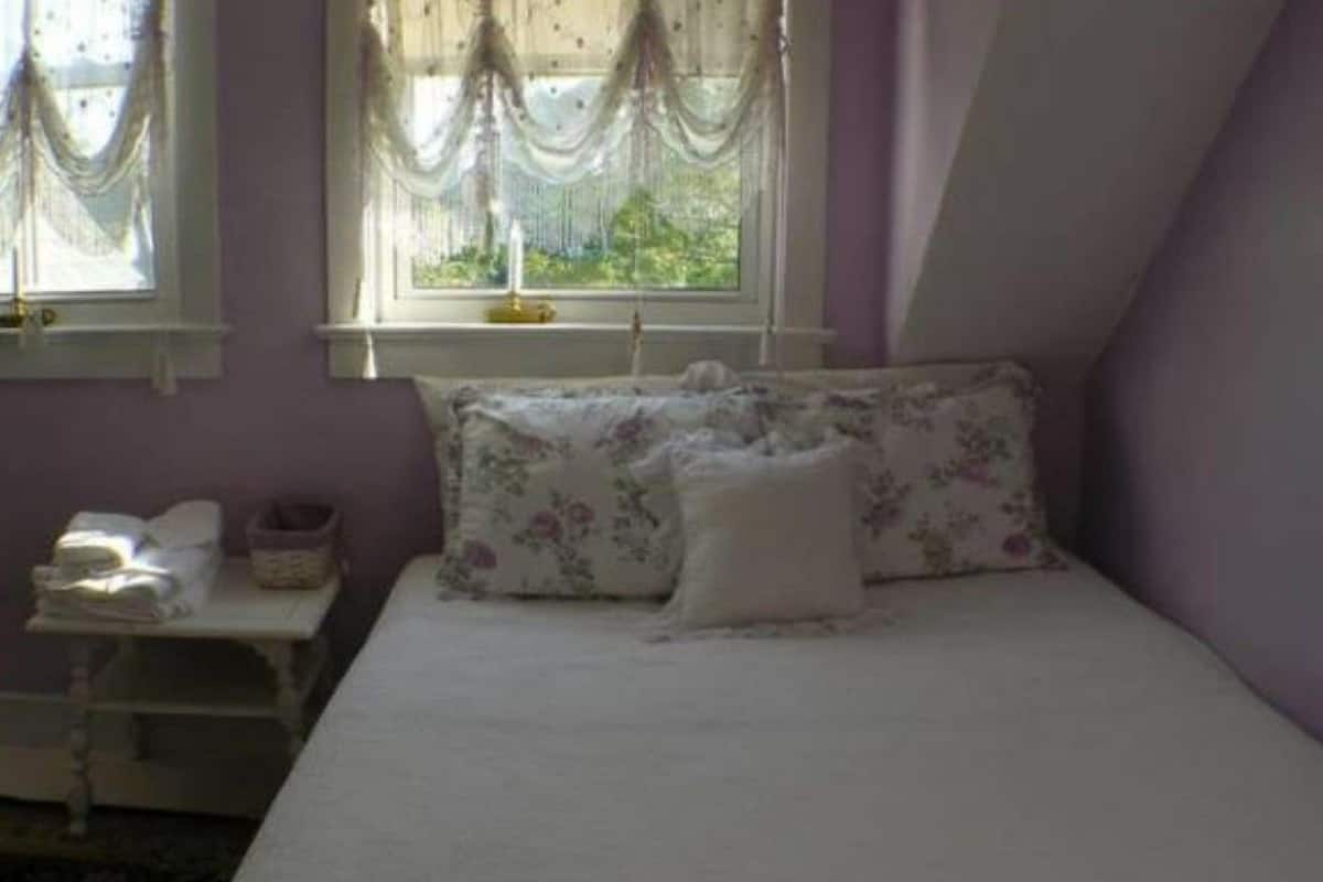 A bedroom with a bed, floral bedding, a nightstand with a lamp, and a window with curtains.