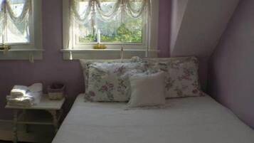 A bedroom with a bed, floral bedding, a nightstand with a lamp, and a window with curtains.