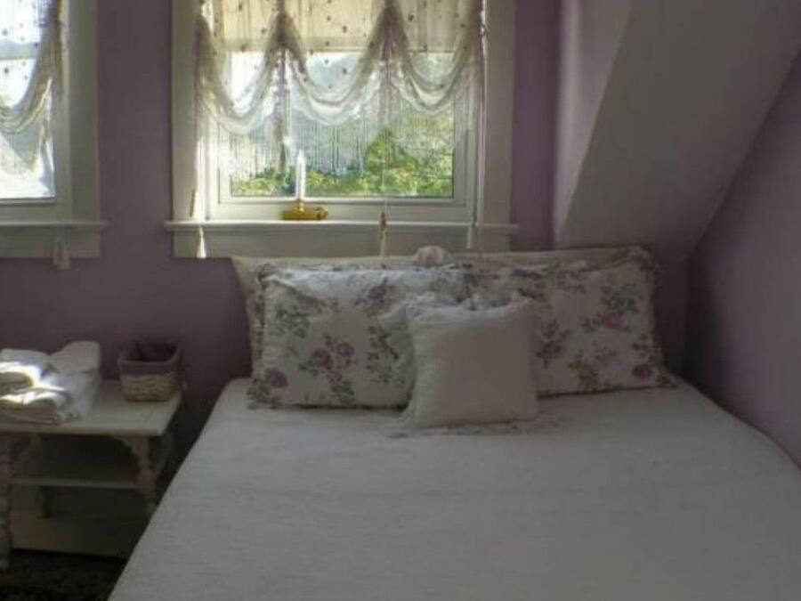 A bedroom with a bed, floral bedding, a nightstand with a lamp, and a window with curtains.