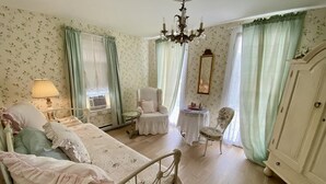 Une chambre à coucher de style vintage, comprenant un lit, une chaise, une petite table et une armoire.