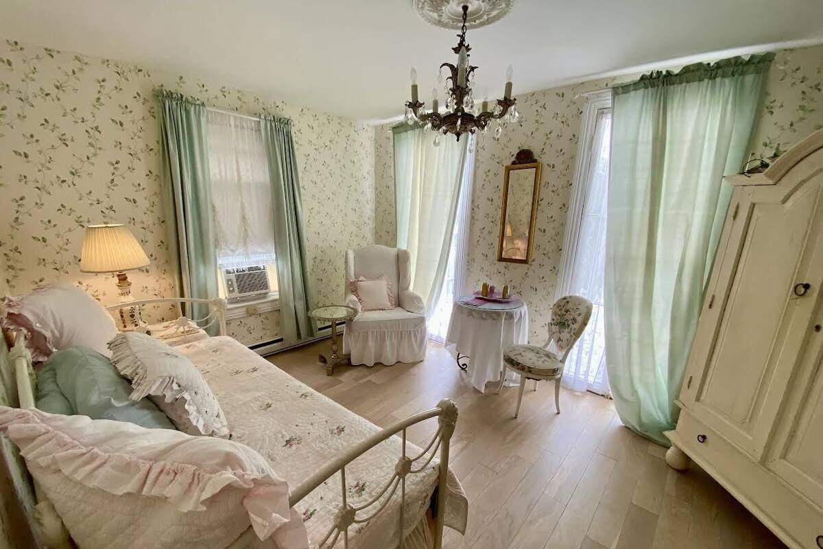 A vintage-style bedroom with a bed, a chair, a small table, and a wardrobe.