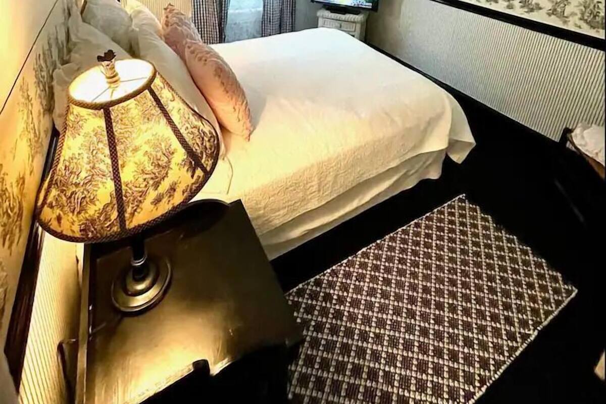 A hotel room with a bed, a lamp, a television, a ceiling fan, and a framed picture on the wall.