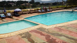 A swimming pool with two sections, lounge chairs, and umbrellas. - Hotel des Deputes (Yaoundé)