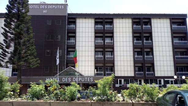 A hotel building with a modern facade, multiple balconies, and a flagpole with flags. - Hotel des Deputes (Yaoundé)