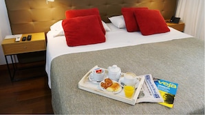 A hotel room with a bed, a bedside table with a lamp, a tray with breakfast items, and a magazine. - IQ Callao by Recoleta Apartments (Buenos Aires)