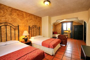 A hotel room with two beds, a chair, a desk, and a view of a balcony.