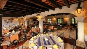 A spacious dining area with multiple tables set for guests, featuring a rustic ceiling and natural light from windows. - Villa Colonial (Antigua Guatemala)