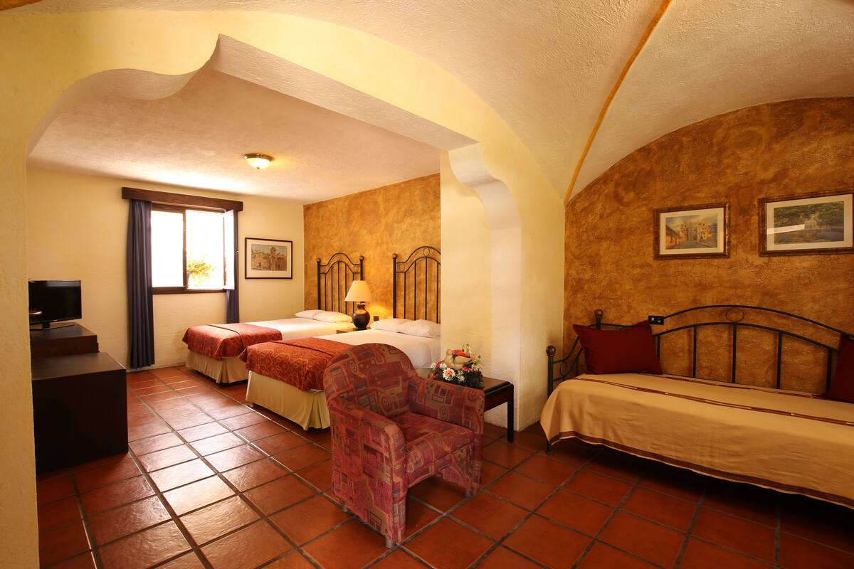 A hotel room with two beds, a chair, a TV, and a window with curtains.