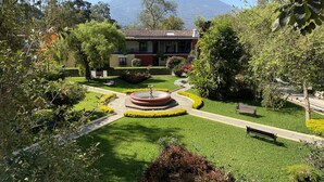 A well-maintained garden with a fountain, benches, and a building with a red roof in the background. - Villa Colonial (Antigua Guatemala)