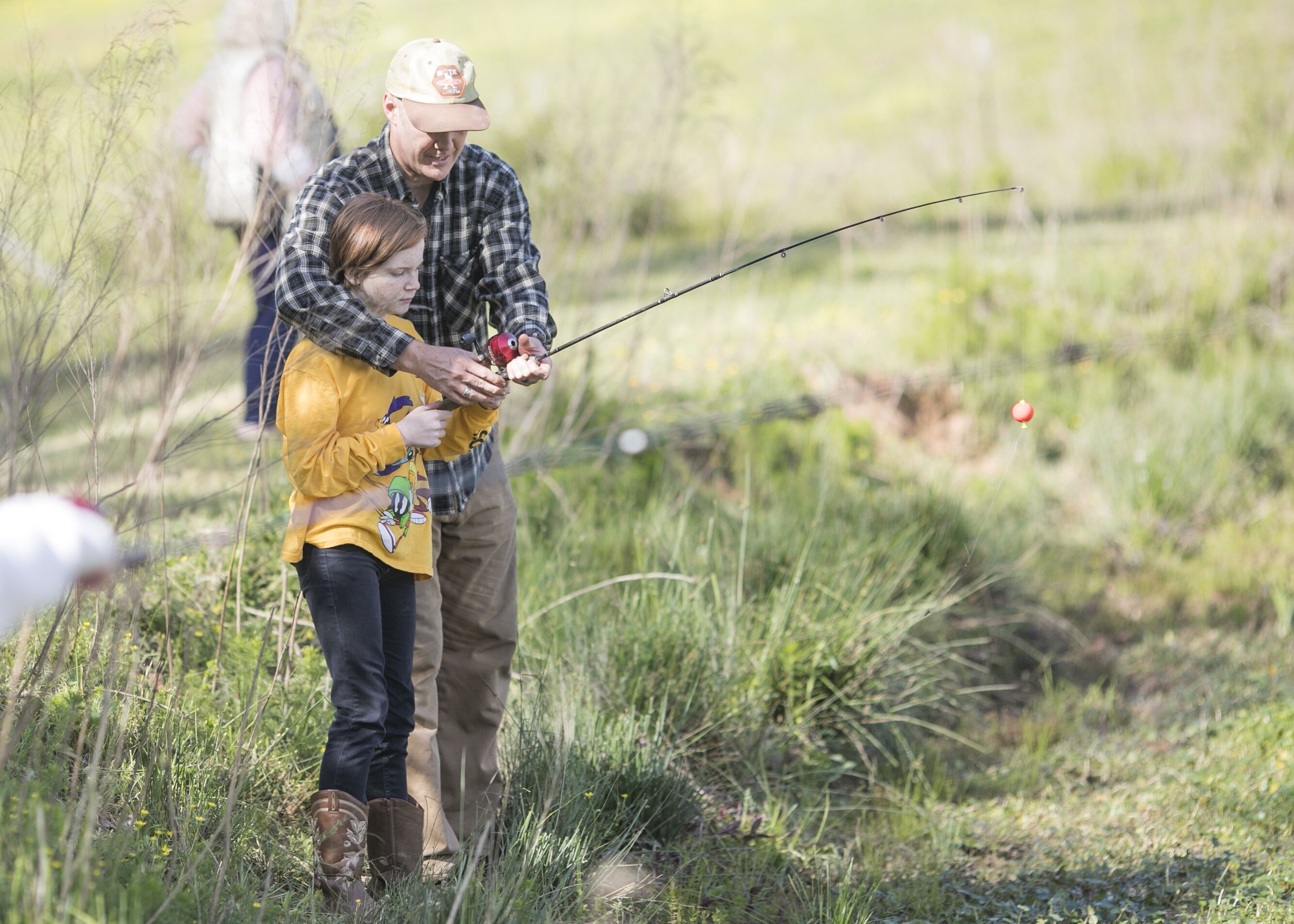 Una persona con camisa y gorro de cuadros pesca con un niño que lleva una camisa amarilla.