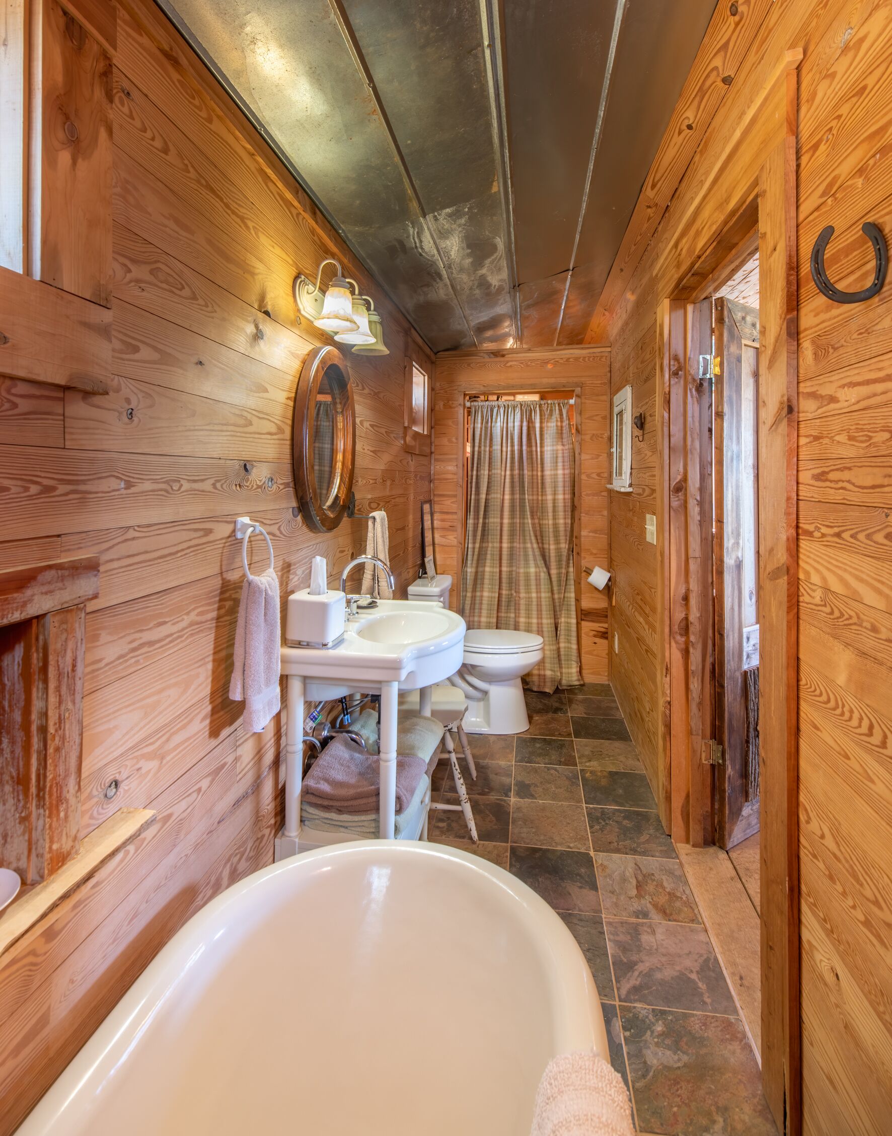 Bagno di una casetta in legno con vasca, due lavabi, un water e una tenda da doccia.
