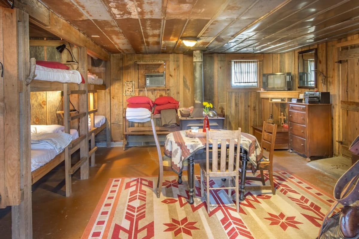 A rustic cabin interior with bunk beds, a dining table, and leather gear.