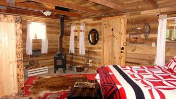 Interior rústico de una cabaña de madera con cama, chimenea, espejo y lámpara colgante.