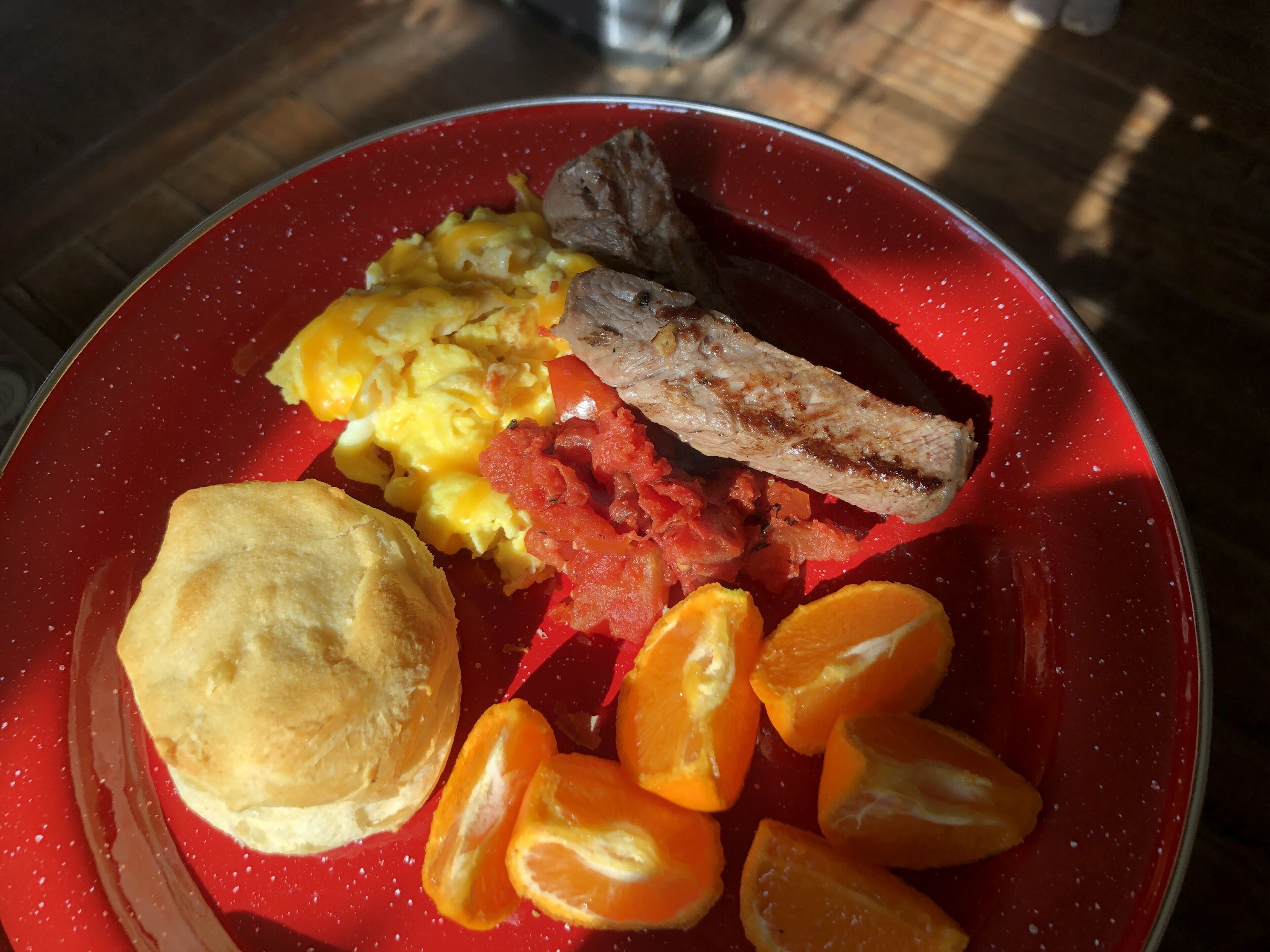 A breakfast plate with scrambled eggs, bacon, orange slices, and a biscuit.