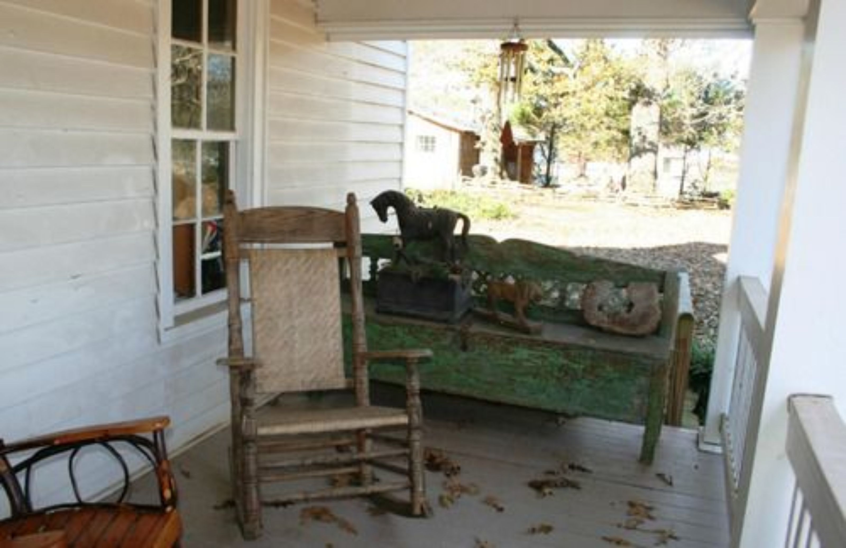 Un porche con una silla y un banco de madera, una escultura decorativa de un caballo y un muro de piedra al fondo.