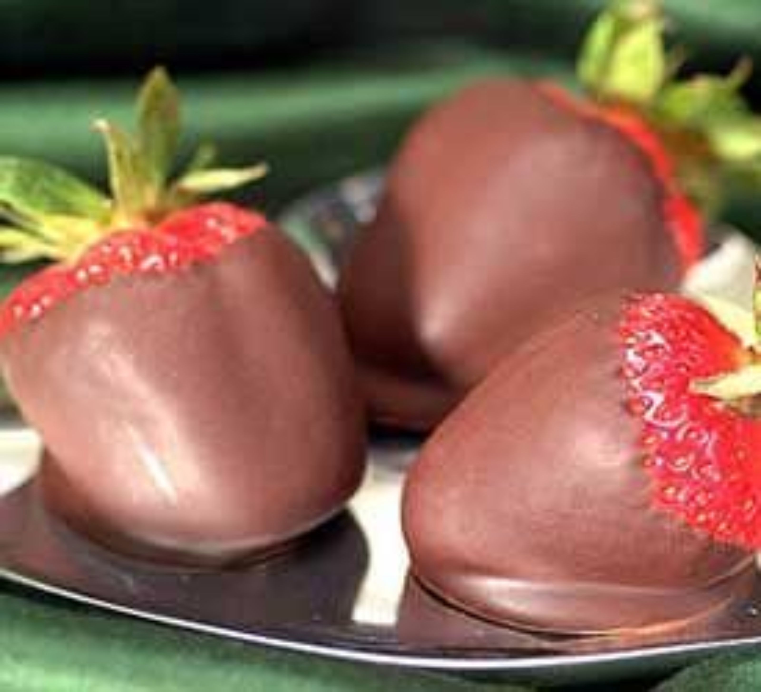 Three strawberries dipped in chocolate on a plate.