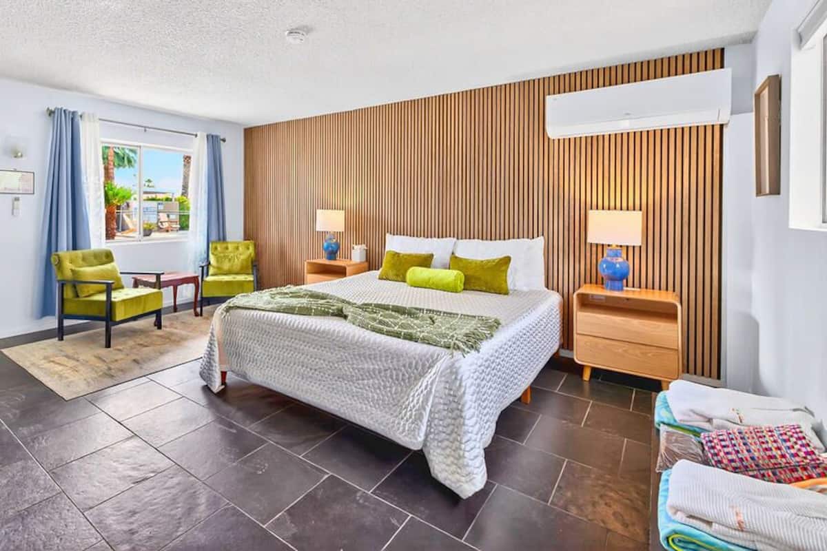A hotel room with a bed, a desk, a chair, a window with curtains, and a wooden wall panel.