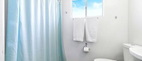 A bathroom with a shower curtain, a toilet, a window, and a towel rack.