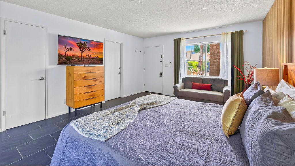 A bedroom with a bed, a dresser, a chair, a window with curtains, and a painting on the wall.