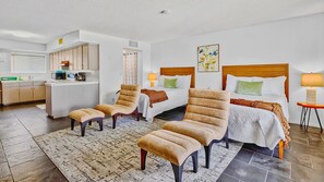 A hotel room with two beds, a kitchenette, a sitting area with chairs and a rug, and a small table with a lamp. - Lido Palms Resort and Spa (Desert Hot Springs)
