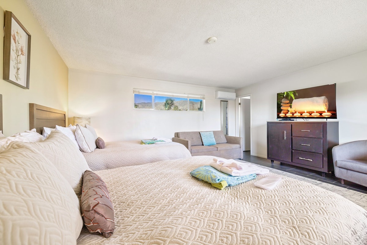 A hotel room with two beds, a sofa, a TV, and a window with a view of mountains.
