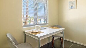 Un comedor con una mesa y sillas, una ventana con persianas y una pequeña obra de arte enmarcada en la pared.