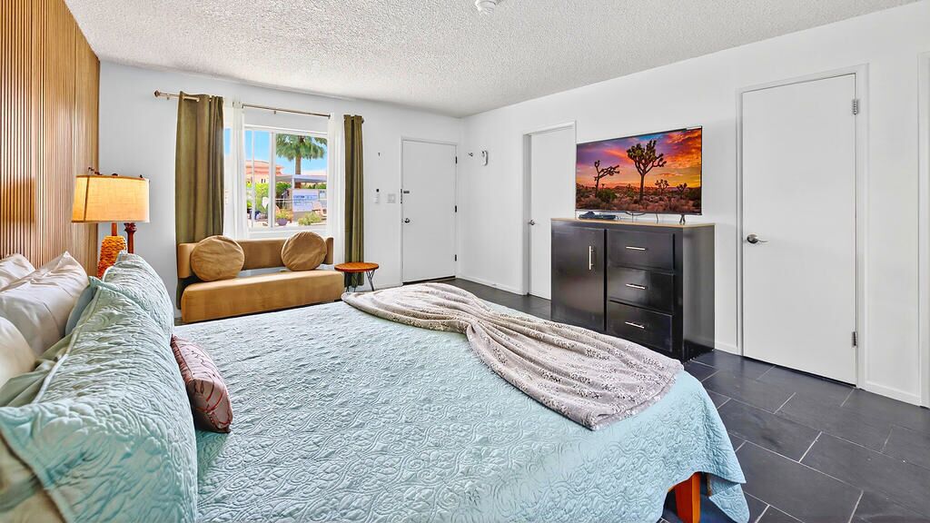 Een hotelkamer met een bed, een bank, een televisie, een kledingkast en een raam met gordijnen.