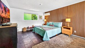 Un dormitorio moderno con cama, mesitas de noche, un escritorio y un cuadro grande en la pared.