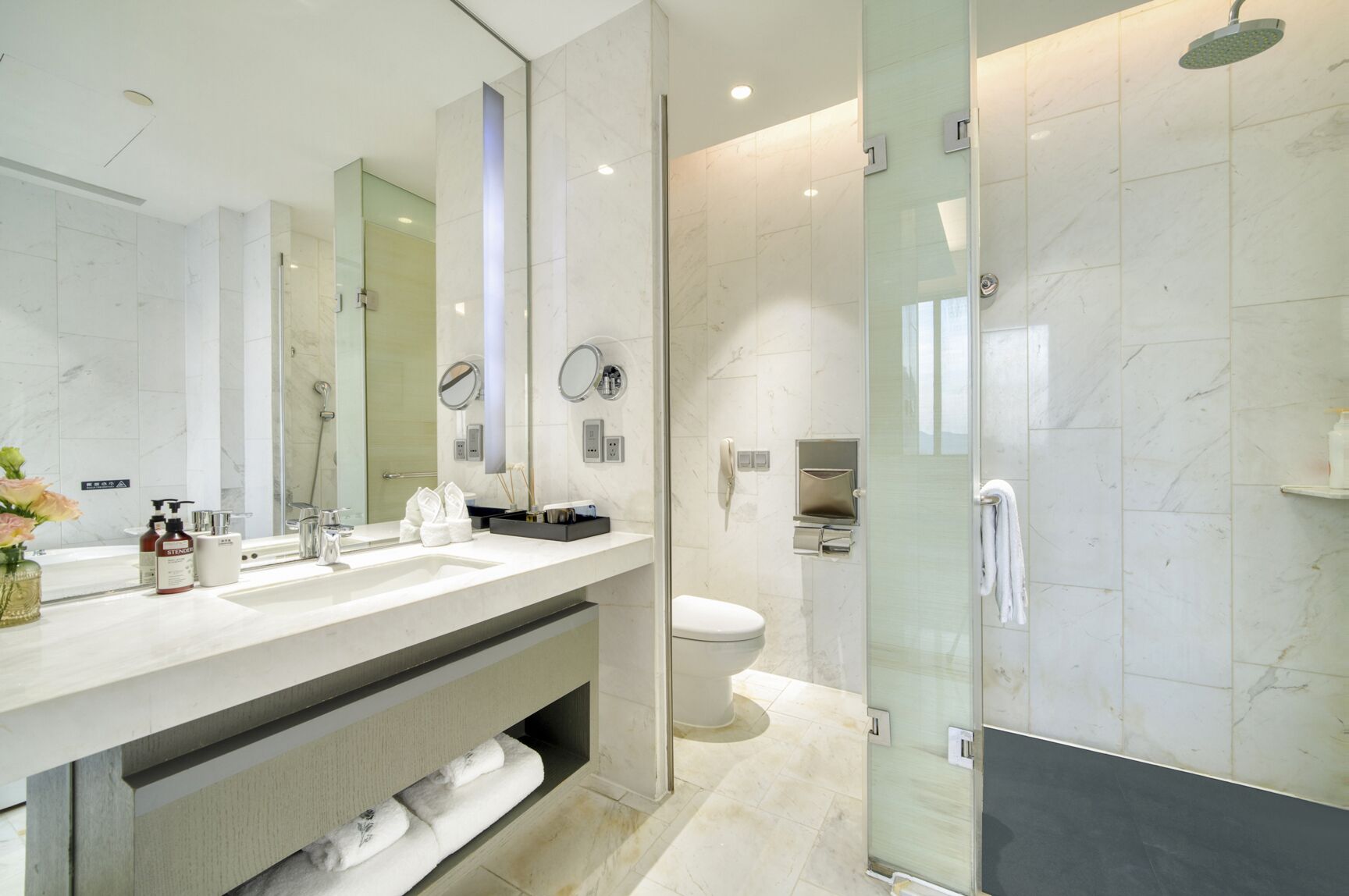 A modern bathroom with a large mirror, a shower, and a toilet.