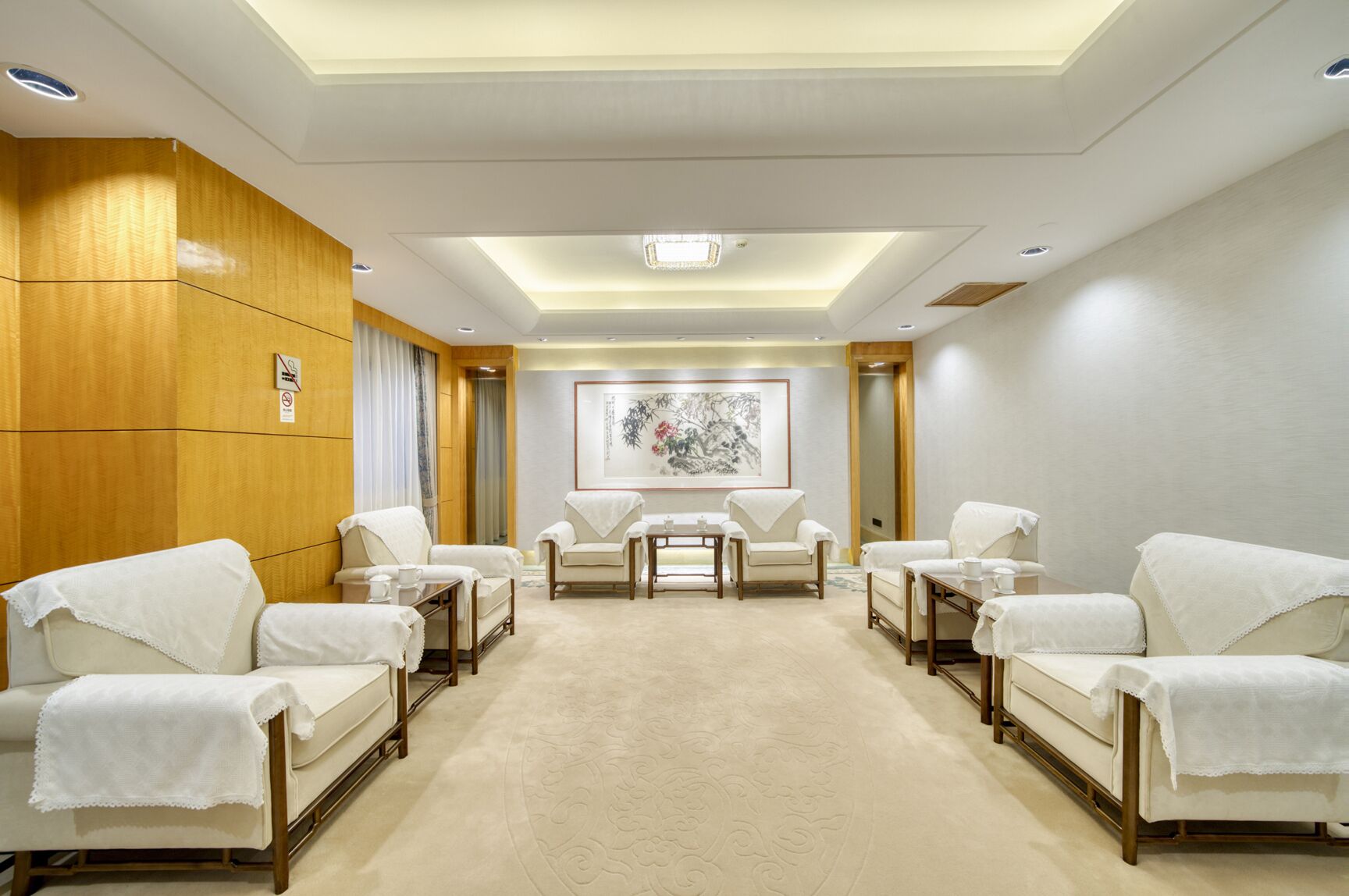 Une pièce comprenant quatre fauteuils blancs, une table centrale et une grande œuvre d’art encadrée accrochée au mur.