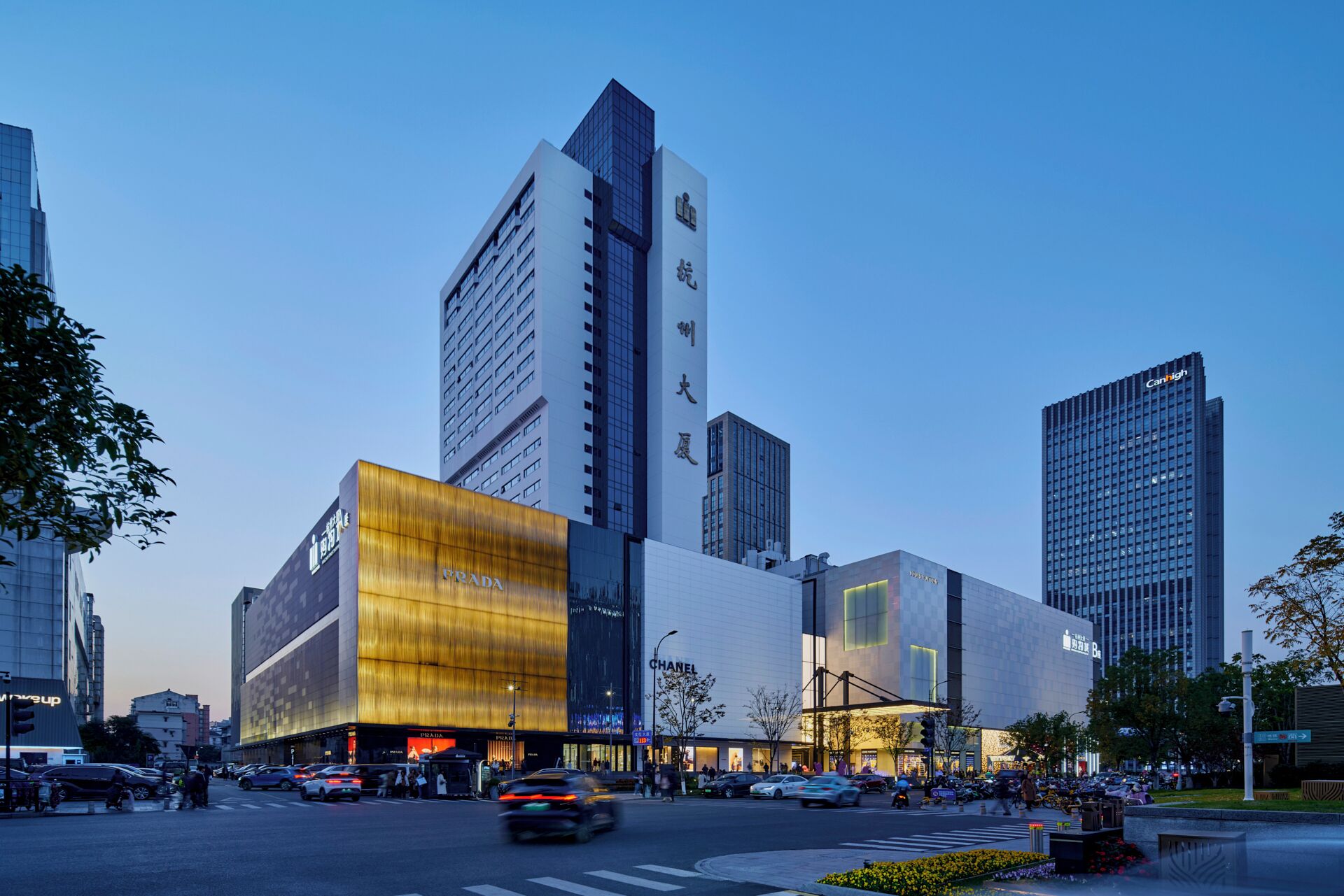A modern urban building with multiple high-rise structures, including a prominent Prada store and a Chanel store.