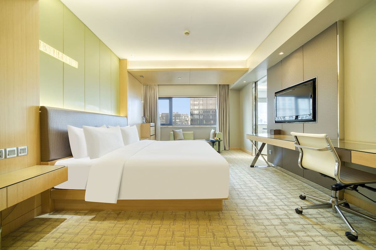 A hotel room with a large bed, a desk, a chair, a television, and a view of the city.