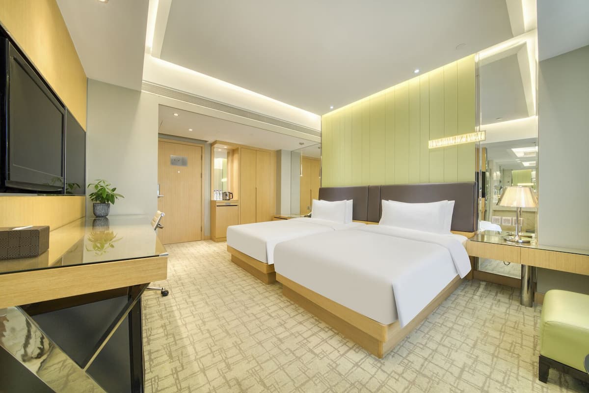 A hotel room with a large bed, a desk with a flat-screen TV, a bedside table, and a mirror.