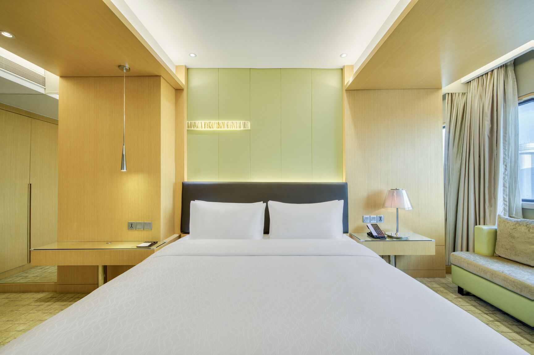 Una camera d'albergo con un letto grande, un comodino con una lampada, un'area salotto e vista sull'esterno.