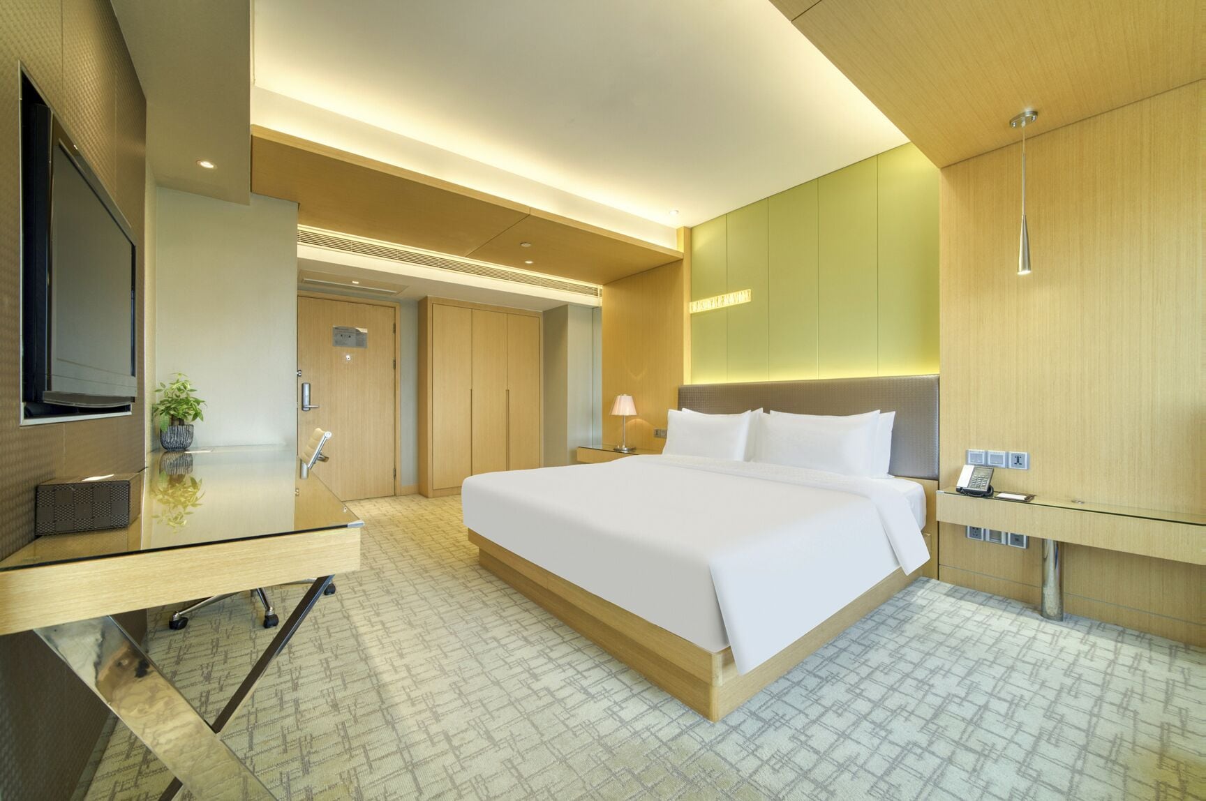 A modern hotel room with a large bed, a desk with a computer, a TV, and a mirror.