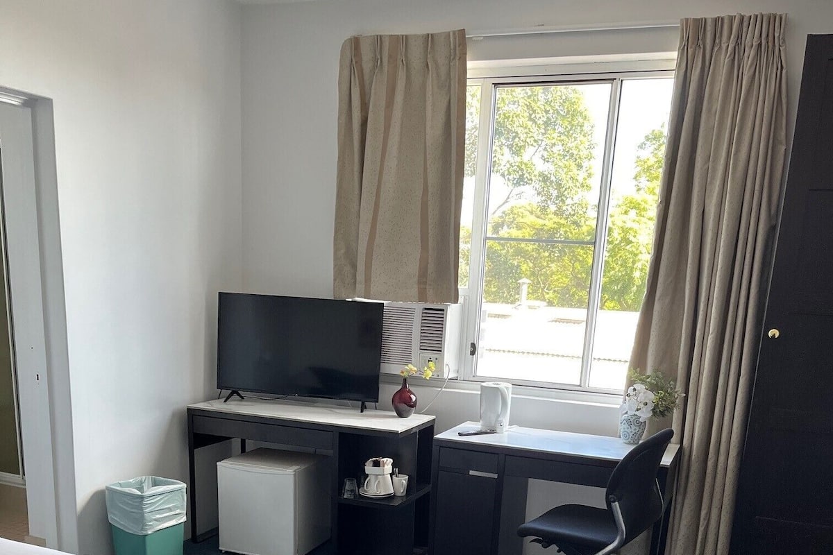 A hotel room with two beds, a desk with a television, a chair, and a window with curtains.