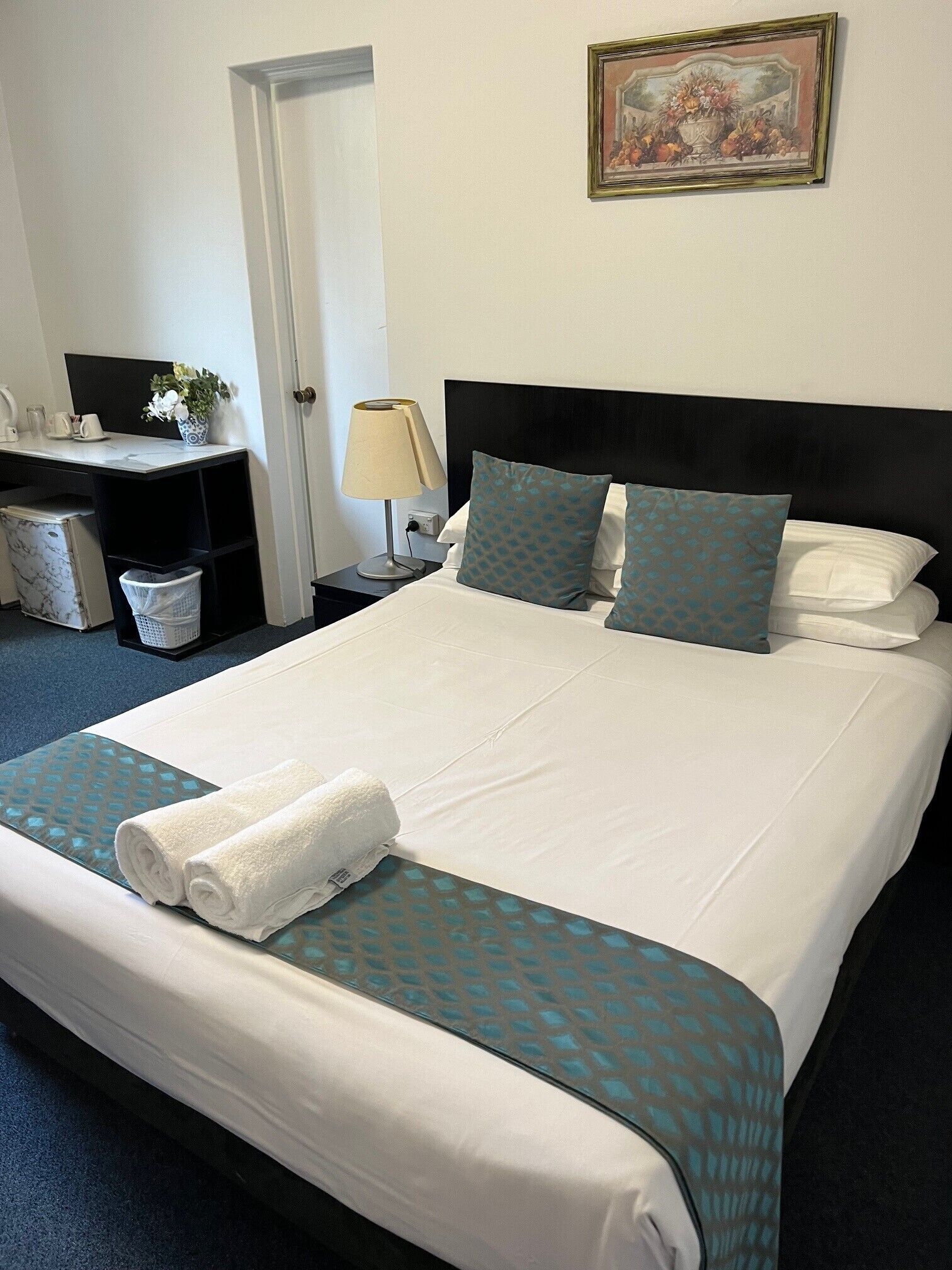 A neatly made bed with a rolled white towel, a black headboard, and patterned pillows.