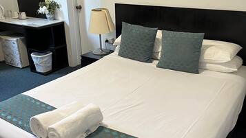 A neatly made bed with a rolled white towel, a black headboard, and patterned pillows.