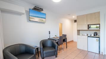 Un espace de vie compact comprenant un coin cuisine, un coin repas avec deux chaises et un téléviseur diffusant une scène de plage.
