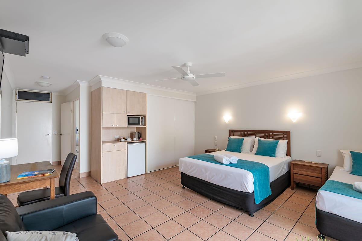 Ein Hotelzimmer mit Bett, Schreibtisch, Stuhl, Mikrowelle und Deckenventilator.