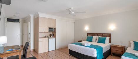 Una habitación de hotel con cama, escritorio, silla, microondas y ventilador de techo.